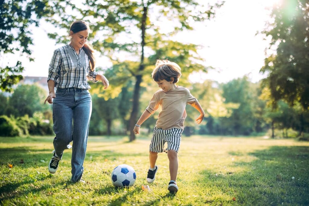 mother son playing soccer in park